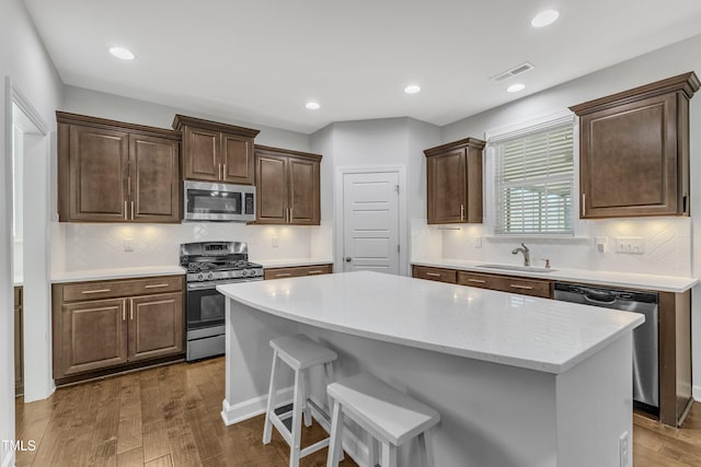 kitchen featuring dark wood-type flooring, appliances with stainless steel finishes, a center island, and sink