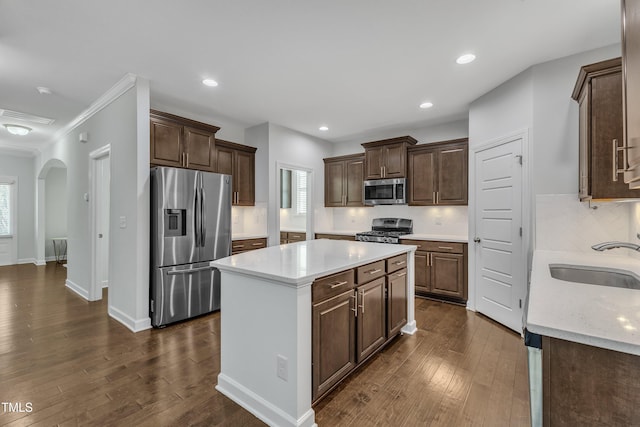 kitchen with sink, dark wood-type flooring, appliances with stainless steel finishes, a kitchen island, and decorative backsplash