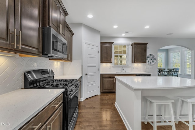 kitchen with dark brown cabinetry, sink, dark hardwood / wood-style floors, stainless steel appliances, and backsplash