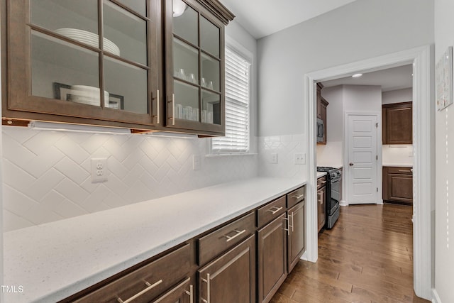 kitchen with black gas range oven, dark brown cabinets, dark wood-type flooring, and tasteful backsplash