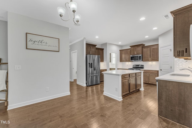 kitchen with sink, appliances with stainless steel finishes, dark hardwood / wood-style flooring, a kitchen island, and decorative backsplash