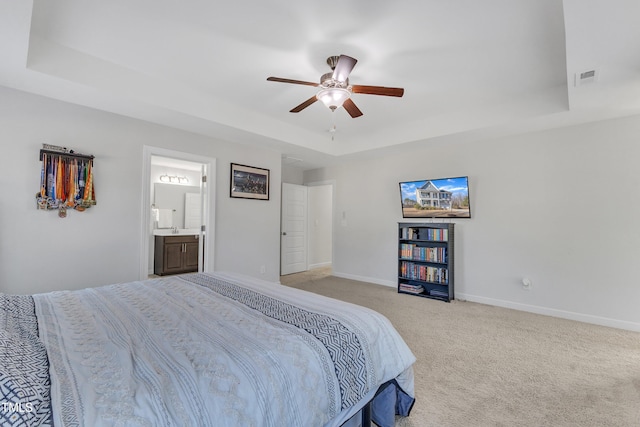 carpeted bedroom with ceiling fan, a raised ceiling, sink, and ensuite bath