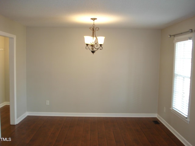 unfurnished room featuring dark hardwood / wood-style flooring, a wealth of natural light, and an inviting chandelier