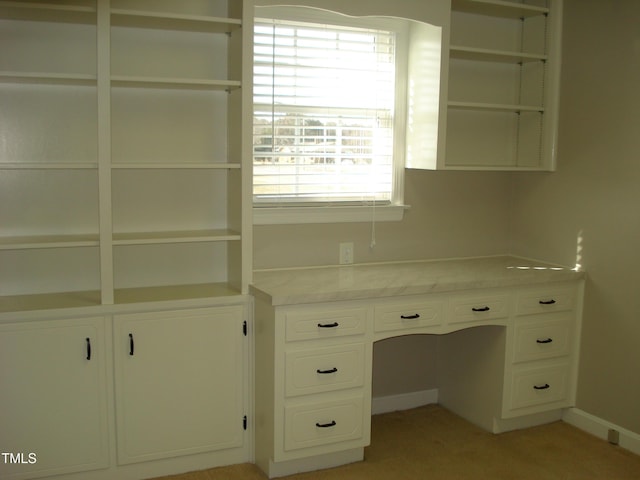 unfurnished office featuring a wealth of natural light, built in desk, and light colored carpet