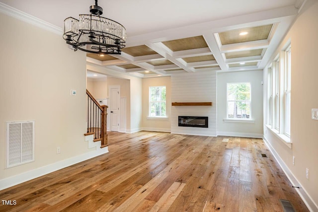 unfurnished living room featuring beamed ceiling, a healthy amount of sunlight, coffered ceiling, and light hardwood / wood-style floors