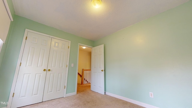 unfurnished bedroom featuring light carpet, a closet, and a textured ceiling