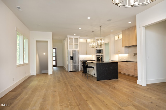 kitchen with appliances with stainless steel finishes, a kitchen island with sink, an inviting chandelier, tasteful backsplash, and light brown cabinetry