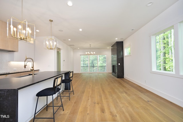 kitchen featuring tasteful backsplash, a breakfast bar area, hanging light fixtures, an inviting chandelier, and light hardwood / wood-style flooring