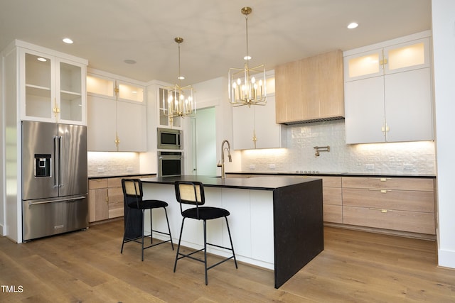 kitchen featuring stainless steel appliances, an island with sink, white cabinets, and light wood-type flooring