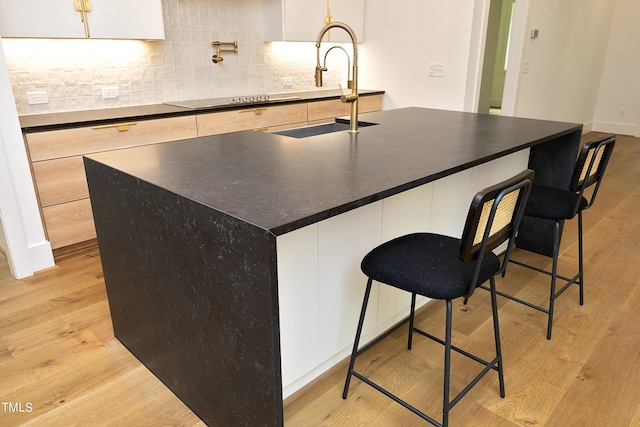 kitchen with white cabinetry, sink, a breakfast bar area, a kitchen island with sink, and light hardwood / wood-style floors