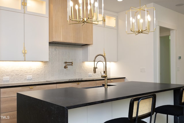 kitchen with decorative light fixtures, tasteful backsplash, a kitchen bar, a chandelier, and a center island with sink