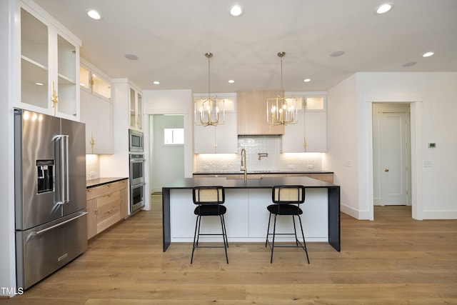 kitchen featuring pendant lighting, appliances with stainless steel finishes, a kitchen island with sink, white cabinets, and light brown cabinetry