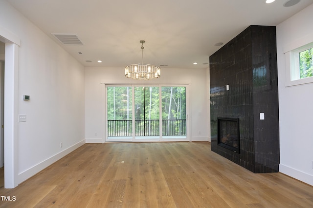 unfurnished living room with a fireplace, a chandelier, and light hardwood / wood-style floors