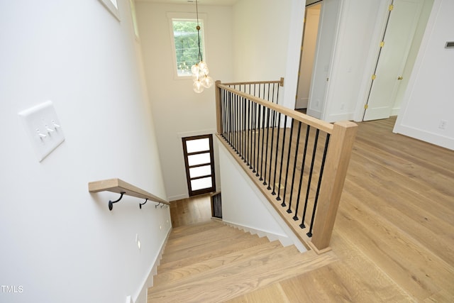 stairway with hardwood / wood-style floors and a notable chandelier