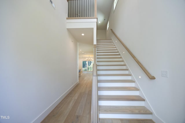 staircase with a towering ceiling, a chandelier, and hardwood / wood-style flooring