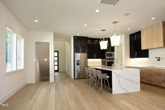 kitchen featuring appliances with stainless steel finishes, a kitchen island with sink, a kitchen breakfast bar, tasteful backsplash, and decorative light fixtures