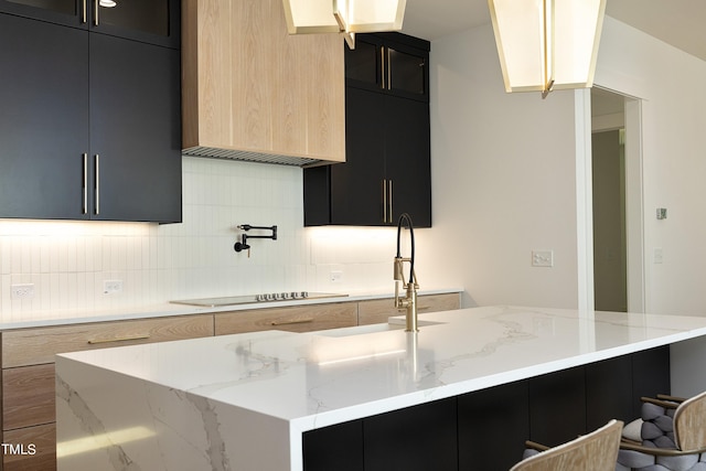 kitchen featuring backsplash, light stone countertops, an island with sink, and light brown cabinets