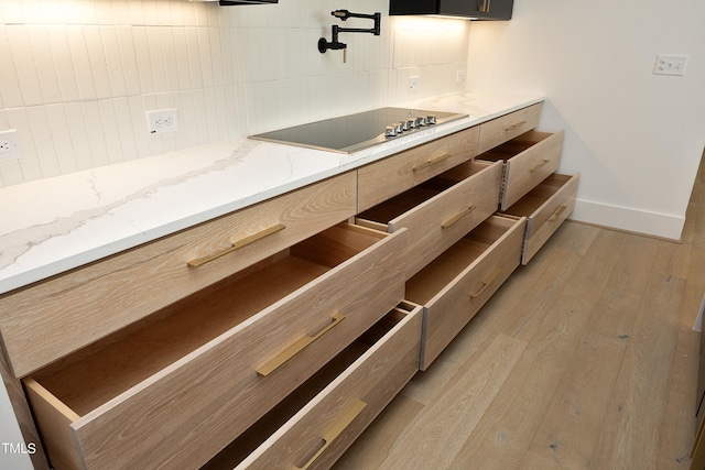 kitchen with light brown cabinets, light wood-type flooring, black electric stovetop, light stone countertops, and backsplash