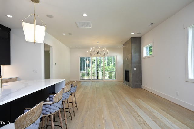 kitchen with a fireplace, decorative light fixtures, a kitchen breakfast bar, light stone counters, and light hardwood / wood-style flooring