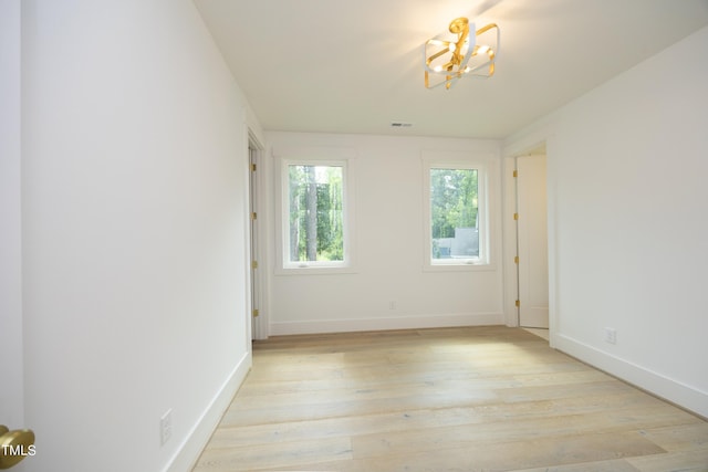 spare room with a notable chandelier and light hardwood / wood-style floors