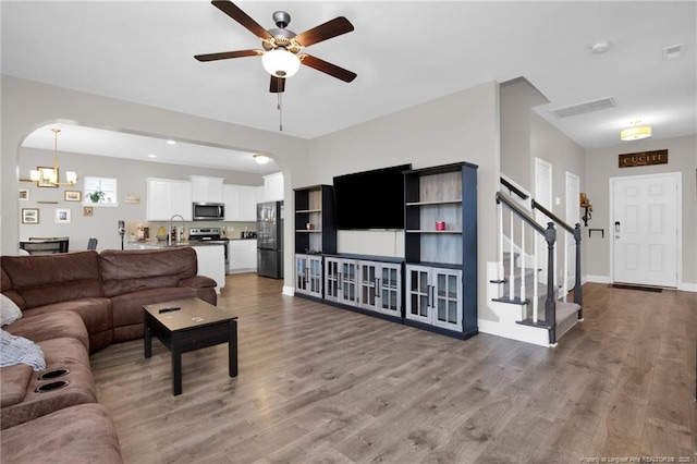 living room featuring ceiling fan with notable chandelier, light hardwood / wood-style floors, and sink