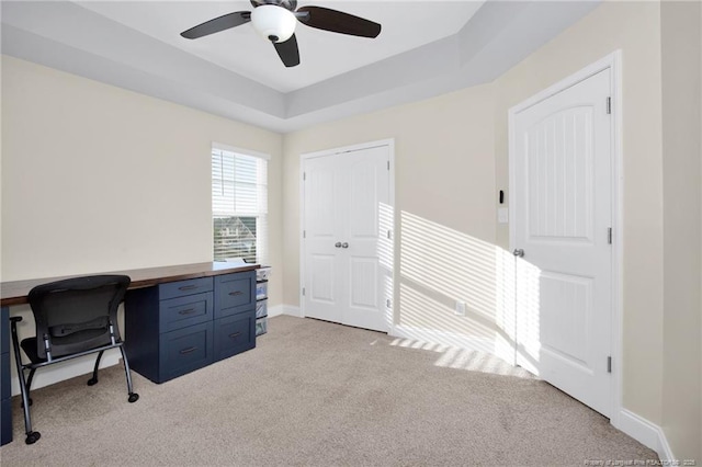 carpeted office featuring a tray ceiling and ceiling fan