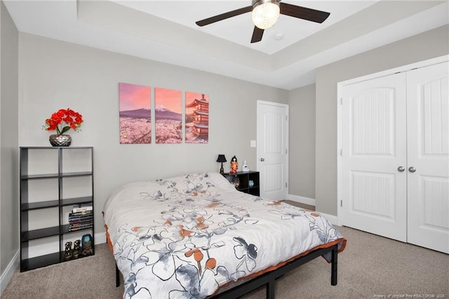 bedroom with ceiling fan, a tray ceiling, carpet floors, and a closet