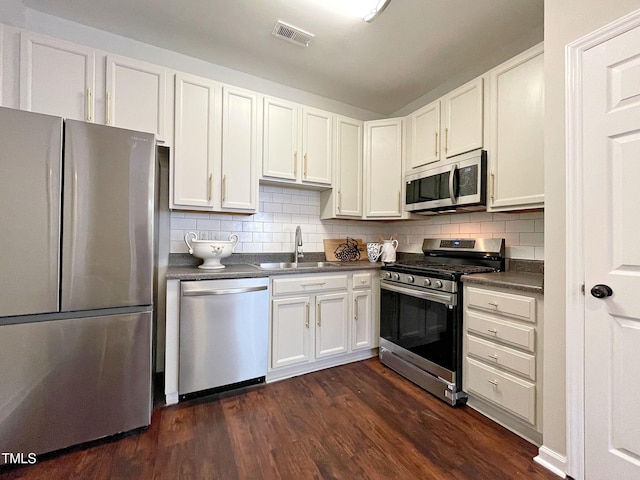 kitchen featuring appliances with stainless steel finishes, white cabinetry, sink, dark hardwood / wood-style flooring, and decorative backsplash