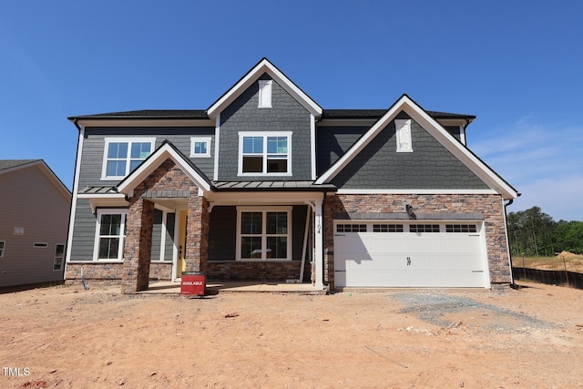 craftsman house with stone siding, dirt driveway, covered porch, a standing seam roof, and an attached garage