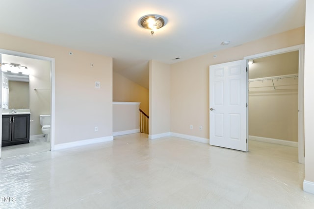 unfurnished bedroom featuring a spacious closet, sink, ensuite bath, and a closet