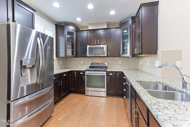 kitchen with stainless steel appliances, sink, backsplash, and light stone counters