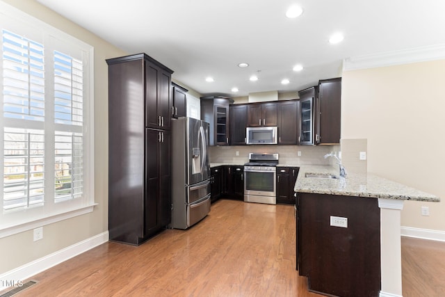 kitchen with sink, decorative backsplash, kitchen peninsula, stainless steel appliances, and light stone countertops