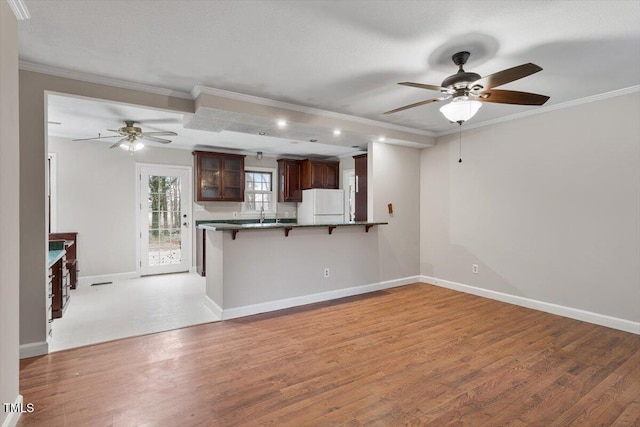 kitchen with light wood-style flooring, ornamental molding, a kitchen breakfast bar, freestanding refrigerator, and a peninsula