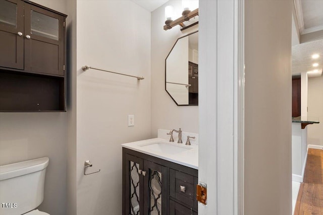 half bathroom featuring toilet, wood finished floors, vanity, and ornamental molding