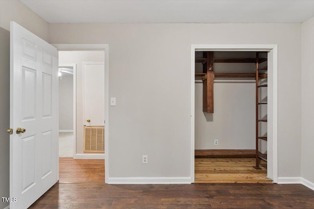 unfurnished bedroom featuring hardwood / wood-style floors, baseboards, visible vents, and a closet