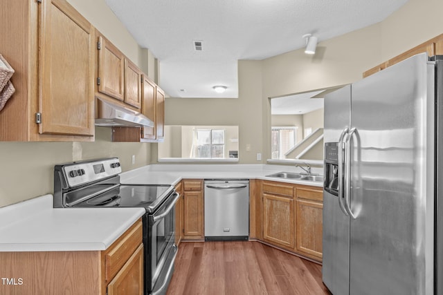 kitchen featuring appliances with stainless steel finishes, sink, a textured ceiling, and light wood-type flooring