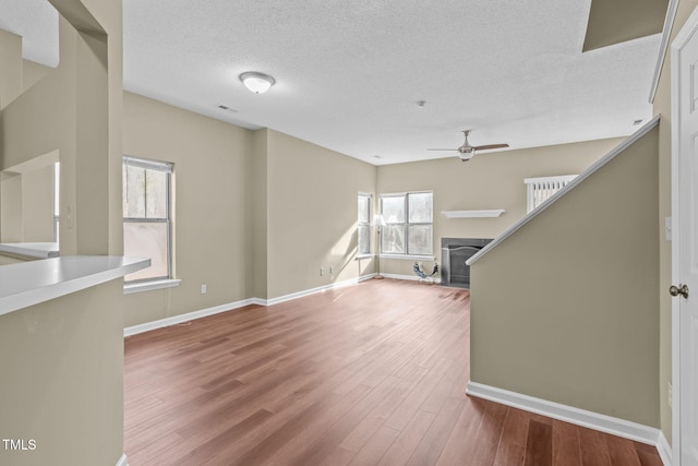 unfurnished living room with hardwood / wood-style flooring, ceiling fan, and a textured ceiling