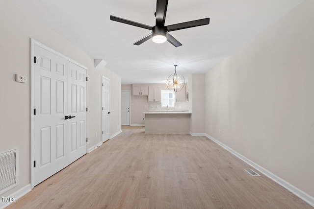 unfurnished living room with sink, ceiling fan with notable chandelier, and light wood-type flooring