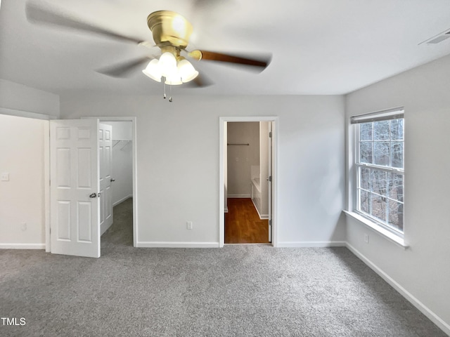 unfurnished bedroom with connected bathroom, a spacious closet, dark carpet, ceiling fan, and a closet