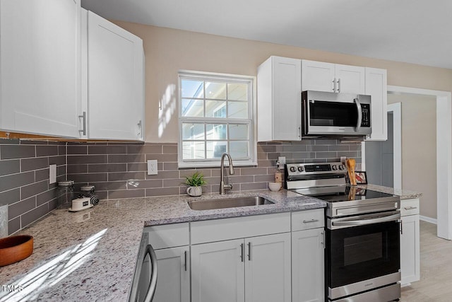 kitchen featuring appliances with stainless steel finishes, light stone countertops, sink, and white cabinets