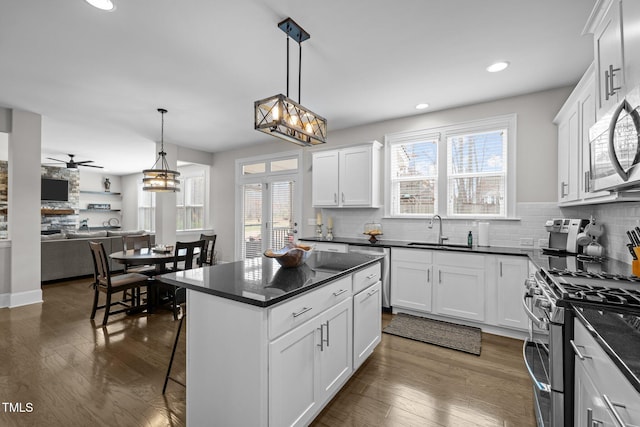 kitchen with decorative light fixtures, a kitchen island, white cabinets, and appliances with stainless steel finishes