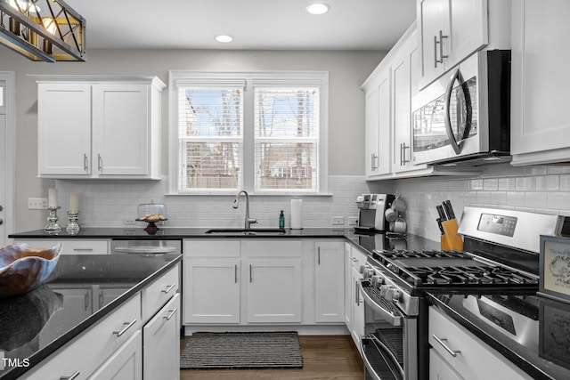 kitchen with sink, dark stone countertops, backsplash, stainless steel appliances, and white cabinets