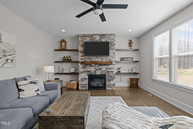 living room with ceiling fan, wood-type flooring, and a stone fireplace