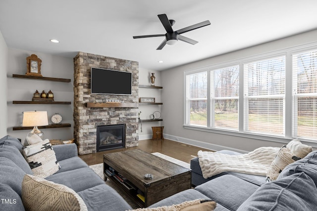 living room with a stone fireplace, a wealth of natural light, ceiling fan, and hardwood / wood-style flooring