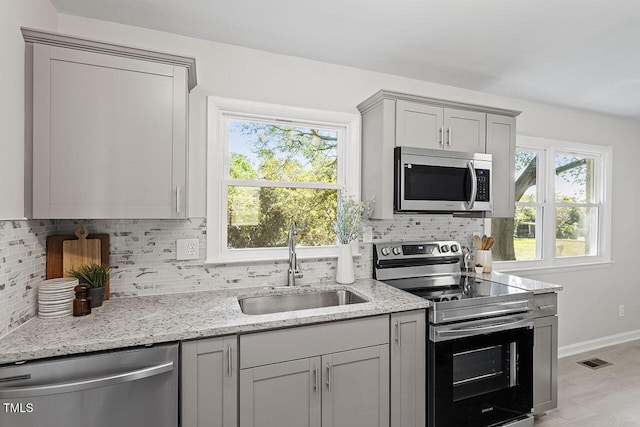 kitchen featuring sink, tasteful backsplash, appliances with stainless steel finishes, gray cabinets, and light stone countertops