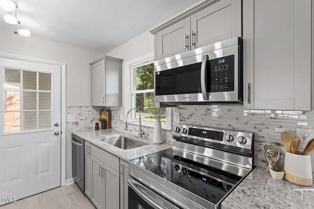 kitchen with sink, gray cabinets, appliances with stainless steel finishes, tasteful backsplash, and light stone countertops