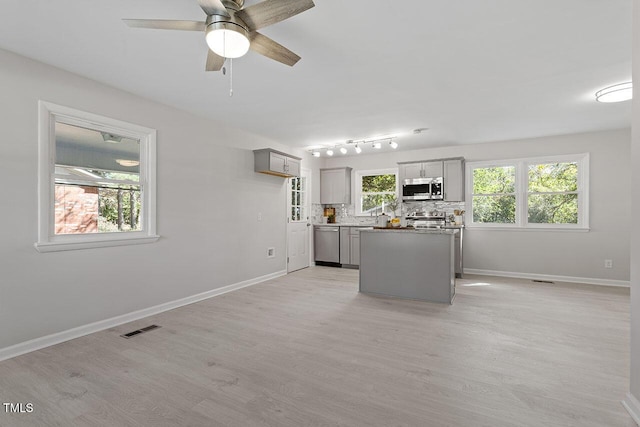 kitchen with gray cabinetry, backsplash, stainless steel appliances, and a center island