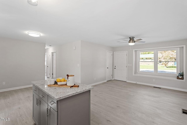 kitchen with light stone counters, gray cabinets, light hardwood / wood-style floors, and a kitchen island