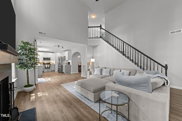 8005 Chatahoochie Ln, Raleigh, NC 27616 - living room featuring a towering ceiling, arched walkways, light wood-style flooring, a fireplace, and stairway