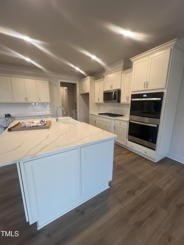 kitchen with sink, appliances with stainless steel finishes, light stone countertops, white cabinets, and a center island with sink